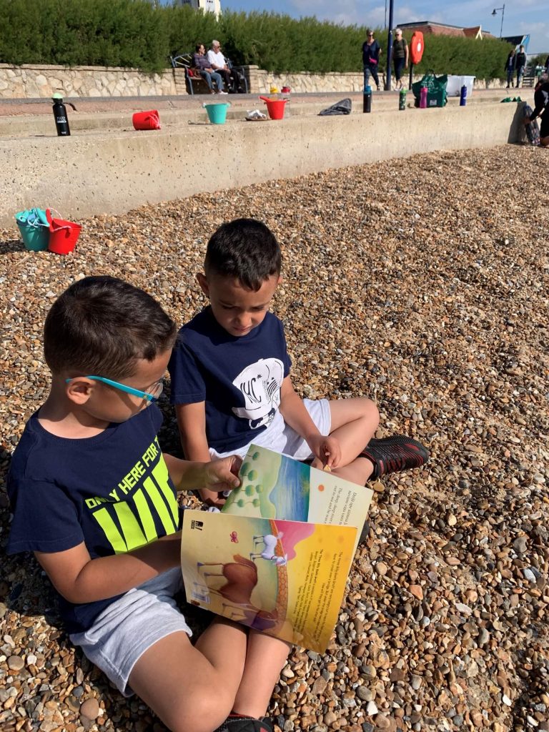 Photo of two pupils reading on a pebbly beach