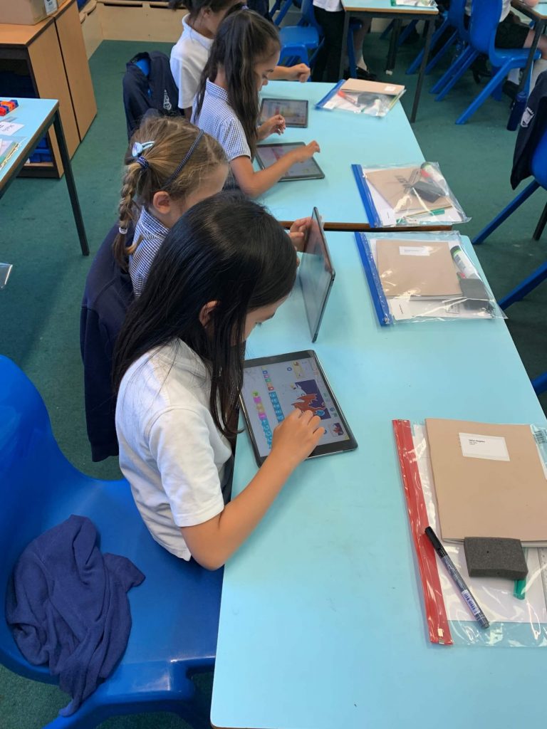 Photo of pupils sitting at a classroom desk working on tablets
